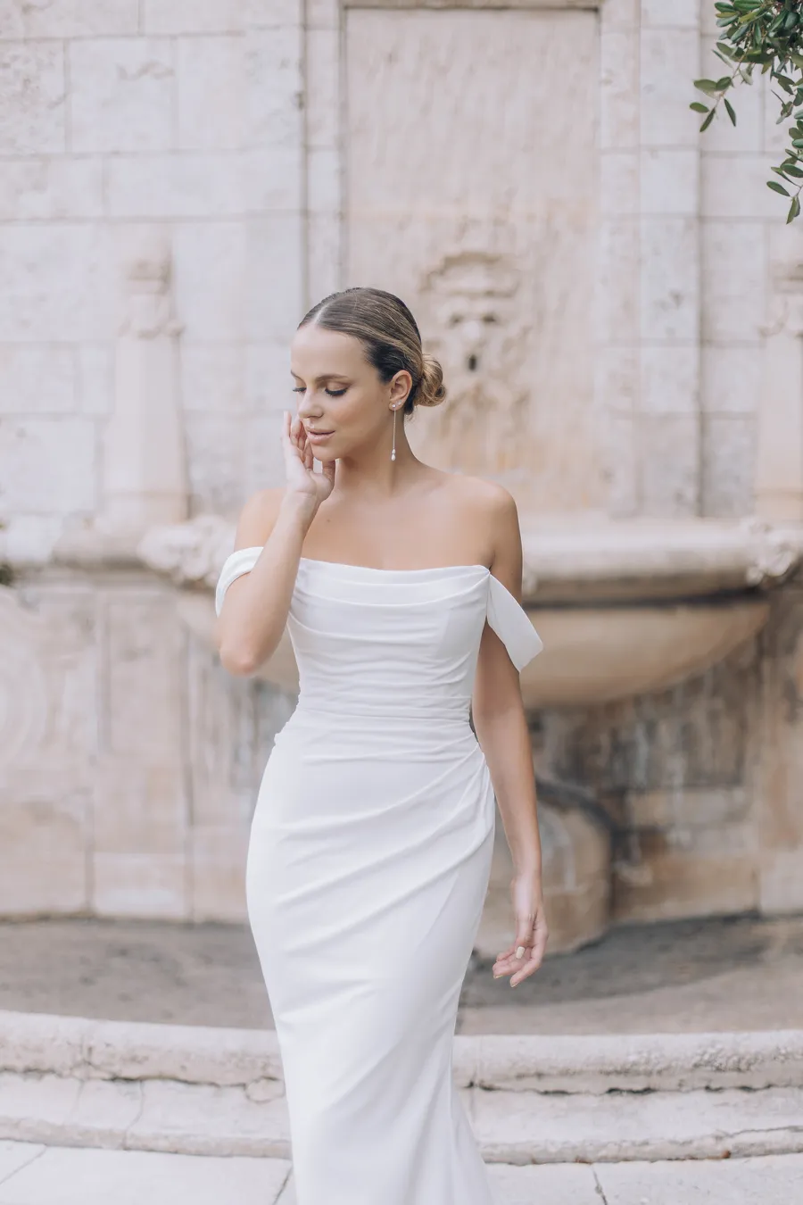 Bride in a modern white gown posing beside pale stone walls