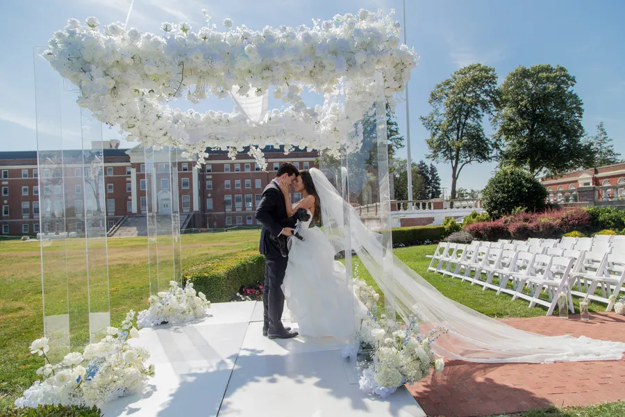 Bride and groom kissing beneath a white floral wedding arch